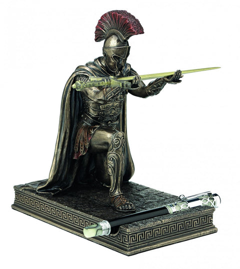 Statue of a warrior in armor with a helmet and cape, holding a spear on a decorative base.